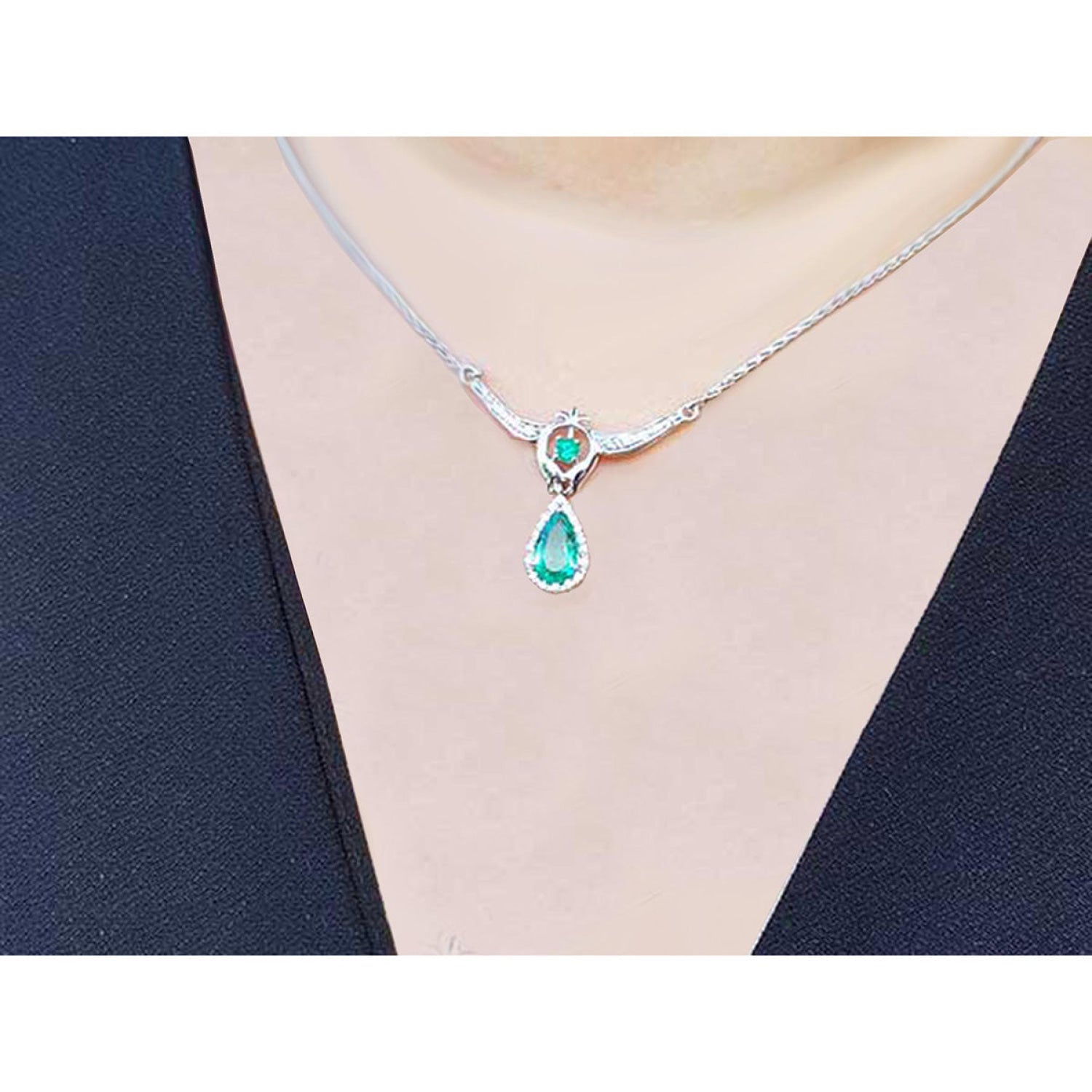 Pear shaped emerald and diamond necklace in 14K white gold on a black top.