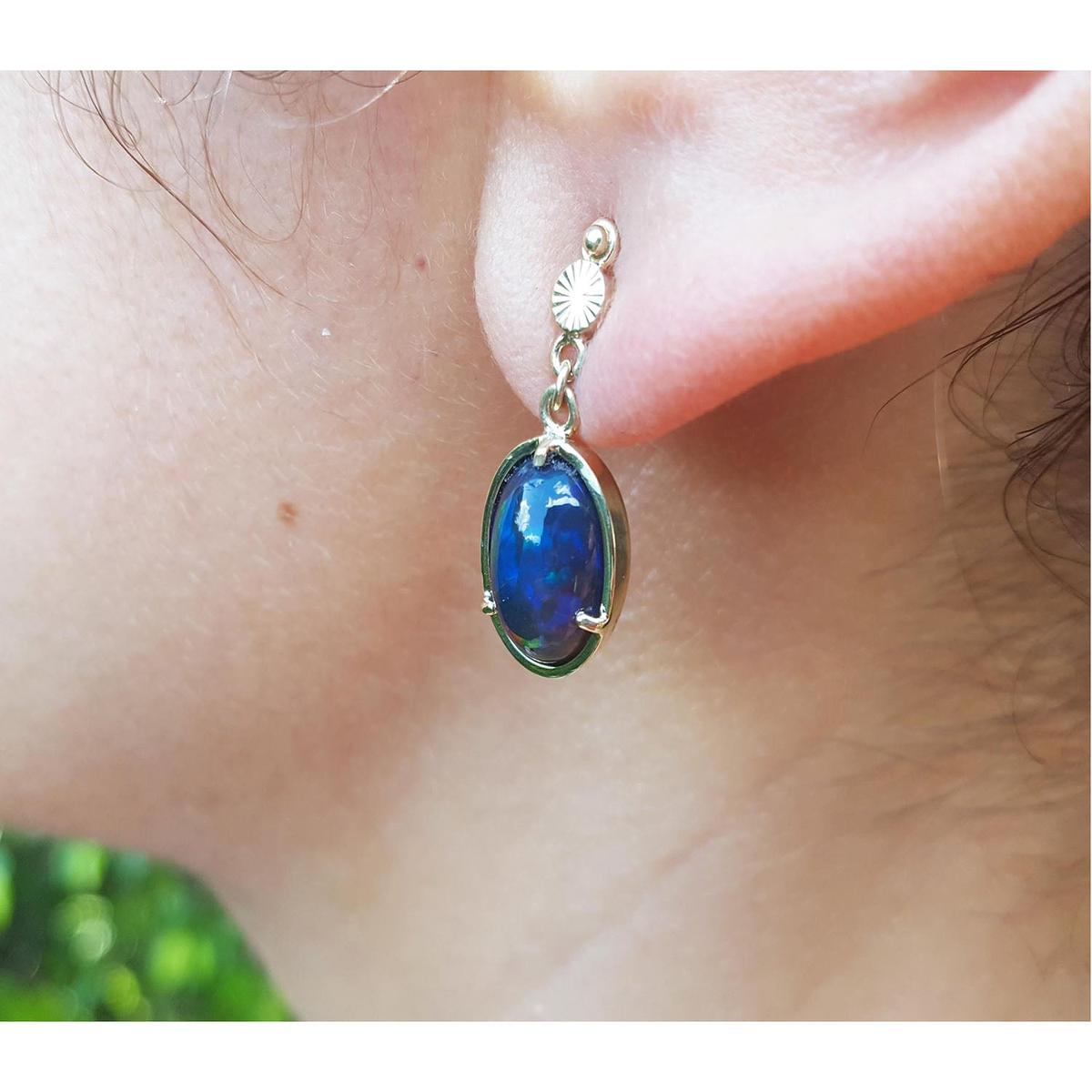 Welo black opal earring worn on an ear with a blurred green background