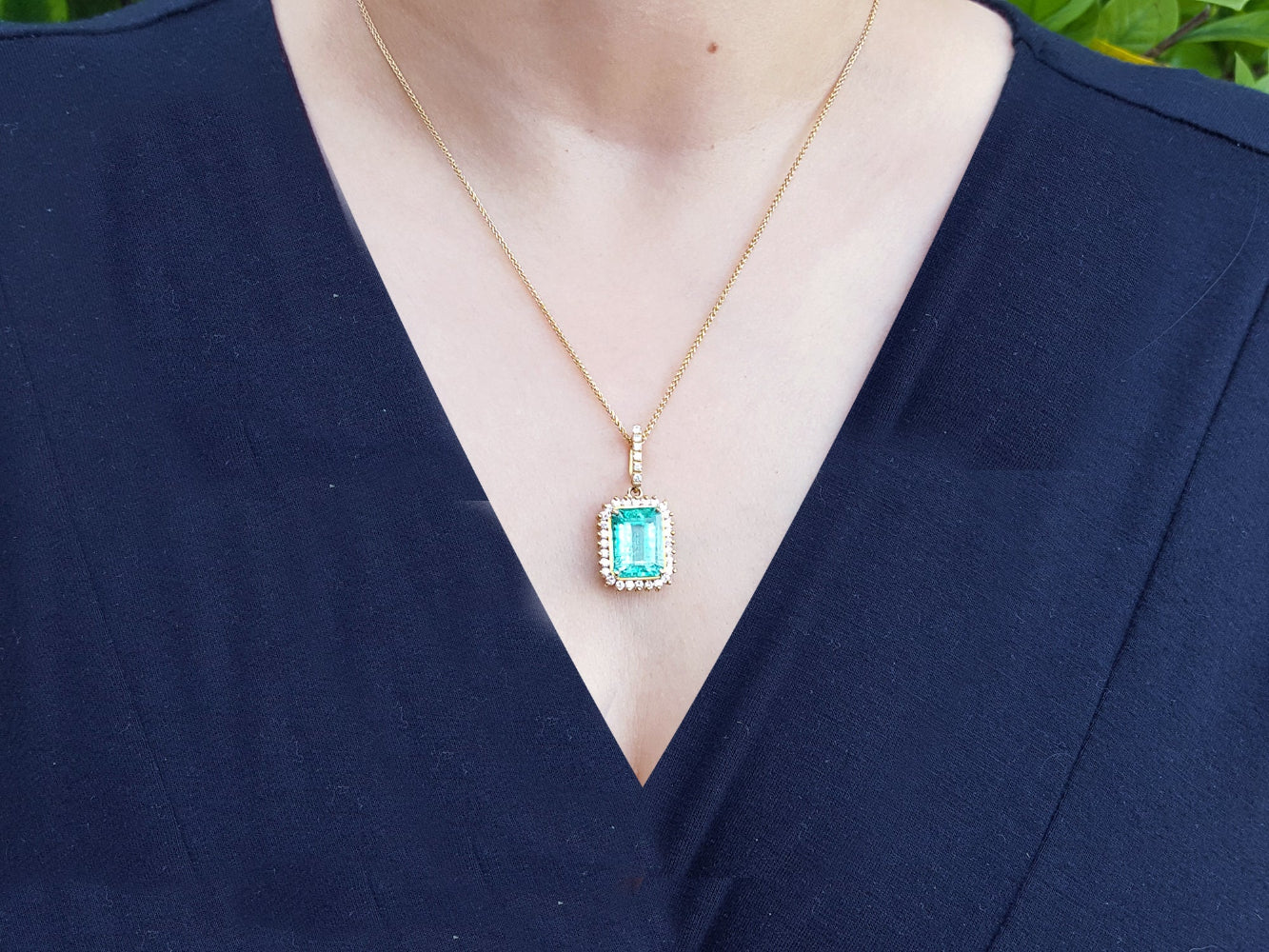 Gold necklace with a natural colombian emerald pendant on a woman wearing a dark blue top.