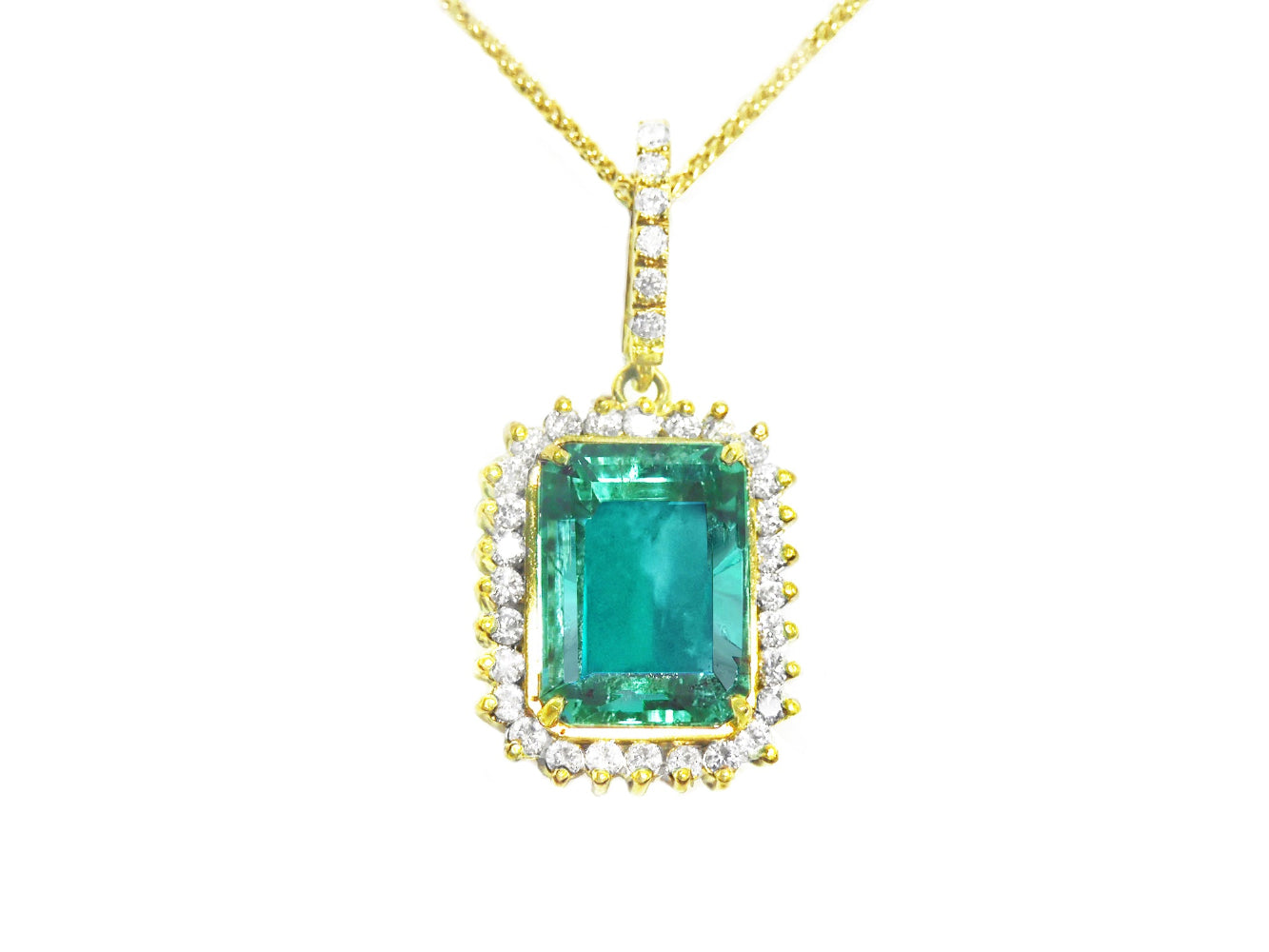 A natural emerald-cut colombian emerald surrounded by a halo diamond pendant in yellow gold.
