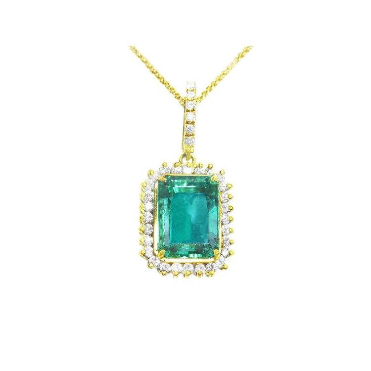 A natural emerald-cut colombian emerald surrounded by a halo diamond pendant in yellow gold.