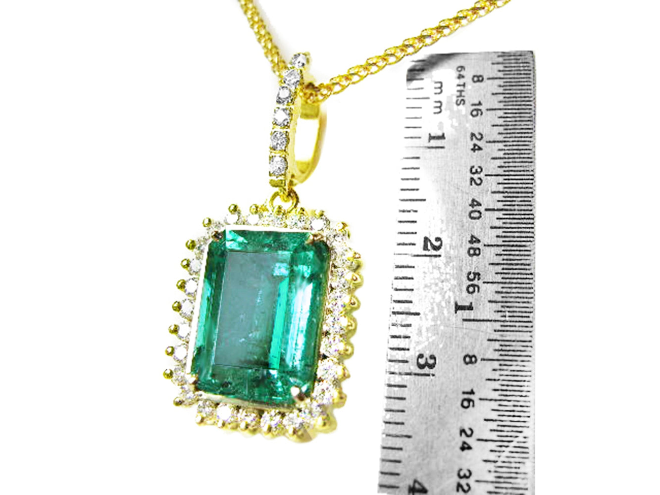 Gold pendant with a natural emerald next to a ruler for scale on a white background.