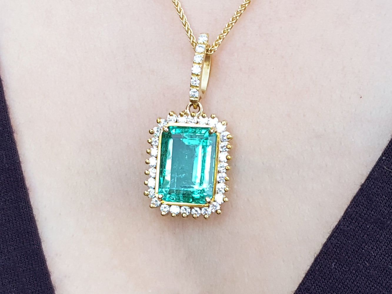 Gold pendant with a square natural emerald on a woman wearing a black top.