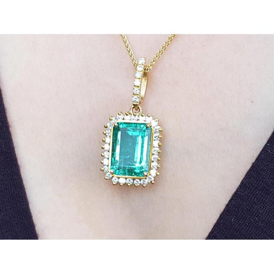 Emerald-cut emerald pendant with halo diamonds in 18K gold, worn on a necklace.