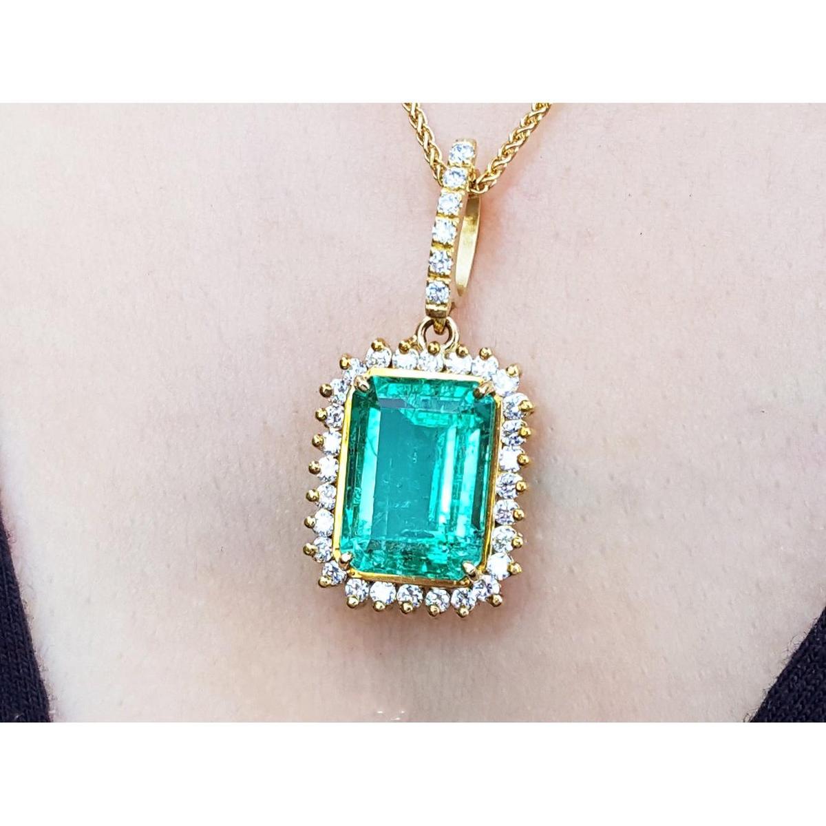 A yellow gold emerald-cut natural emerald pendant with a halo diamond on a person's neck.