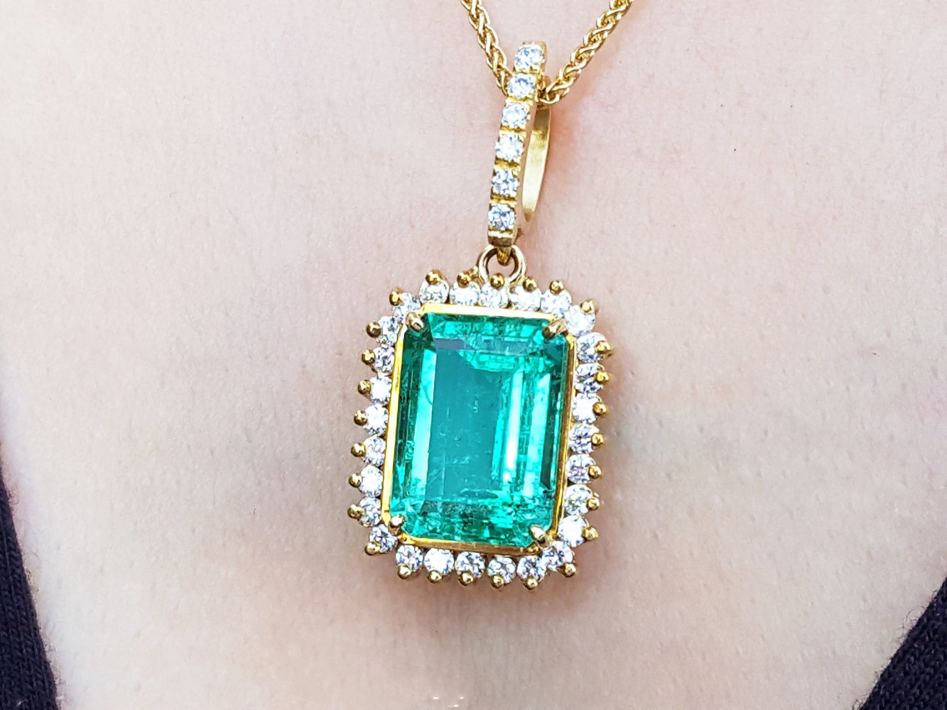 A yellow gold emerald-cut natural emerald pendant with a halo diamond on a person's neck.