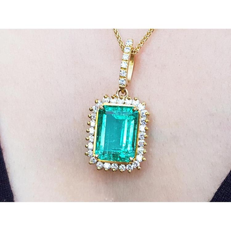 A yellow gold emerald-cut natural emerald pendant with a halo diamond on a person's neck.