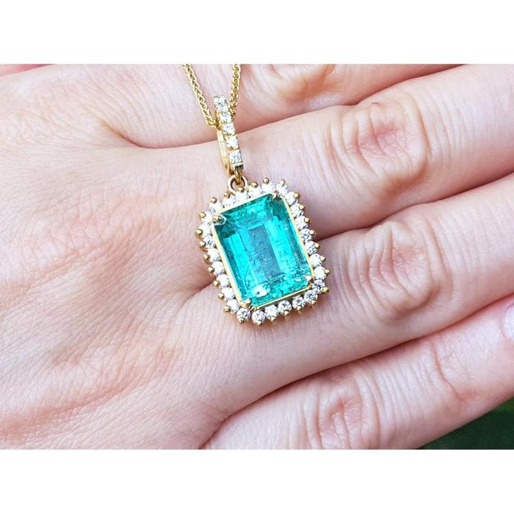 Emerald-cut emerald pendant with halo diamonds in 18K gold, worn on a hand.