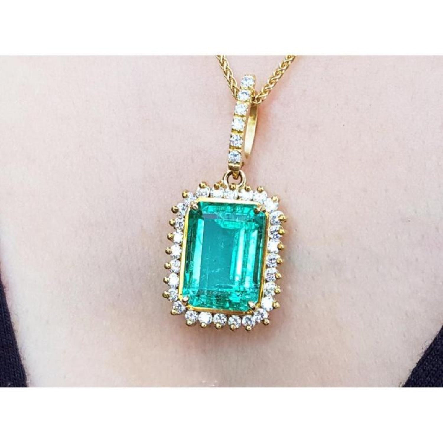 A 18k yellow gold emerald-cut natural emerald pendant with a halo diamond on a person's neck.