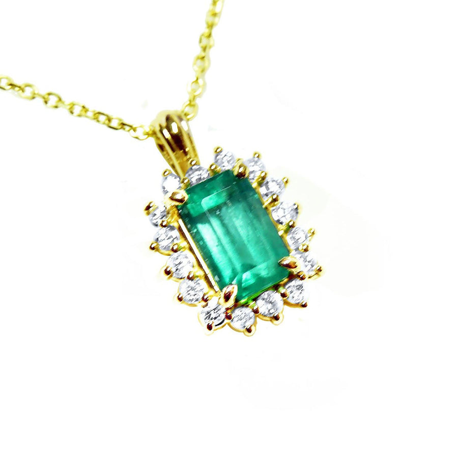 A 14k yellow gold pendant necklace featuring a rectangular emerald-cut colombian emerald surrounded by a halo of diamonds.