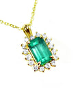 A 14k yellow gold pendant necklace featuring a rectangular emerald-cut colombian emerald surrounded by a halo of diamonds.