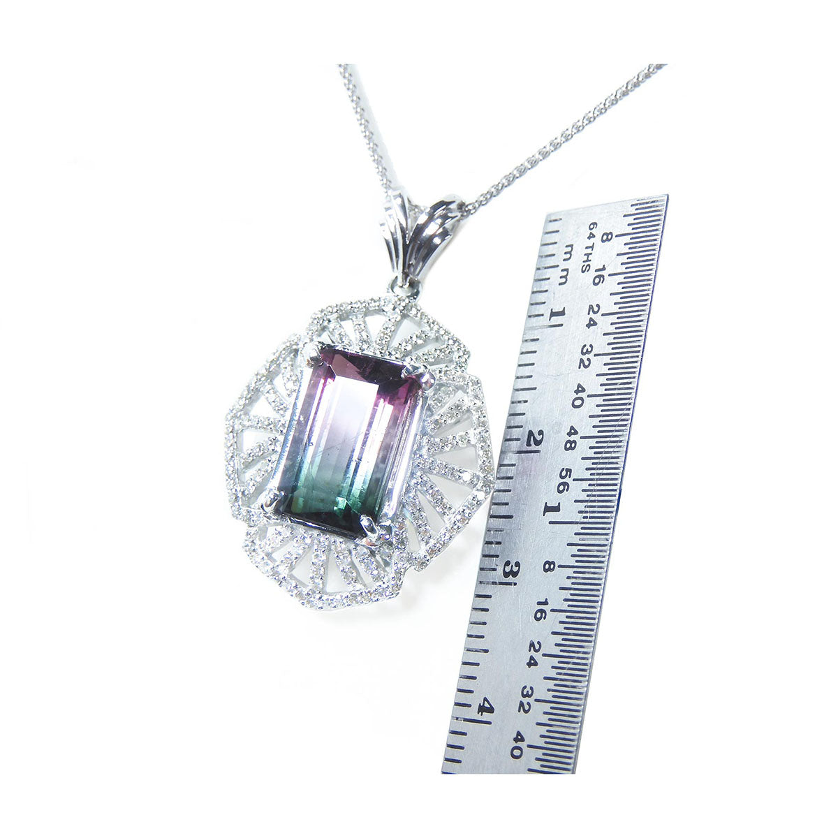 A brazilian watermelon tourmaline pendant with a ruler for scale on a white background.