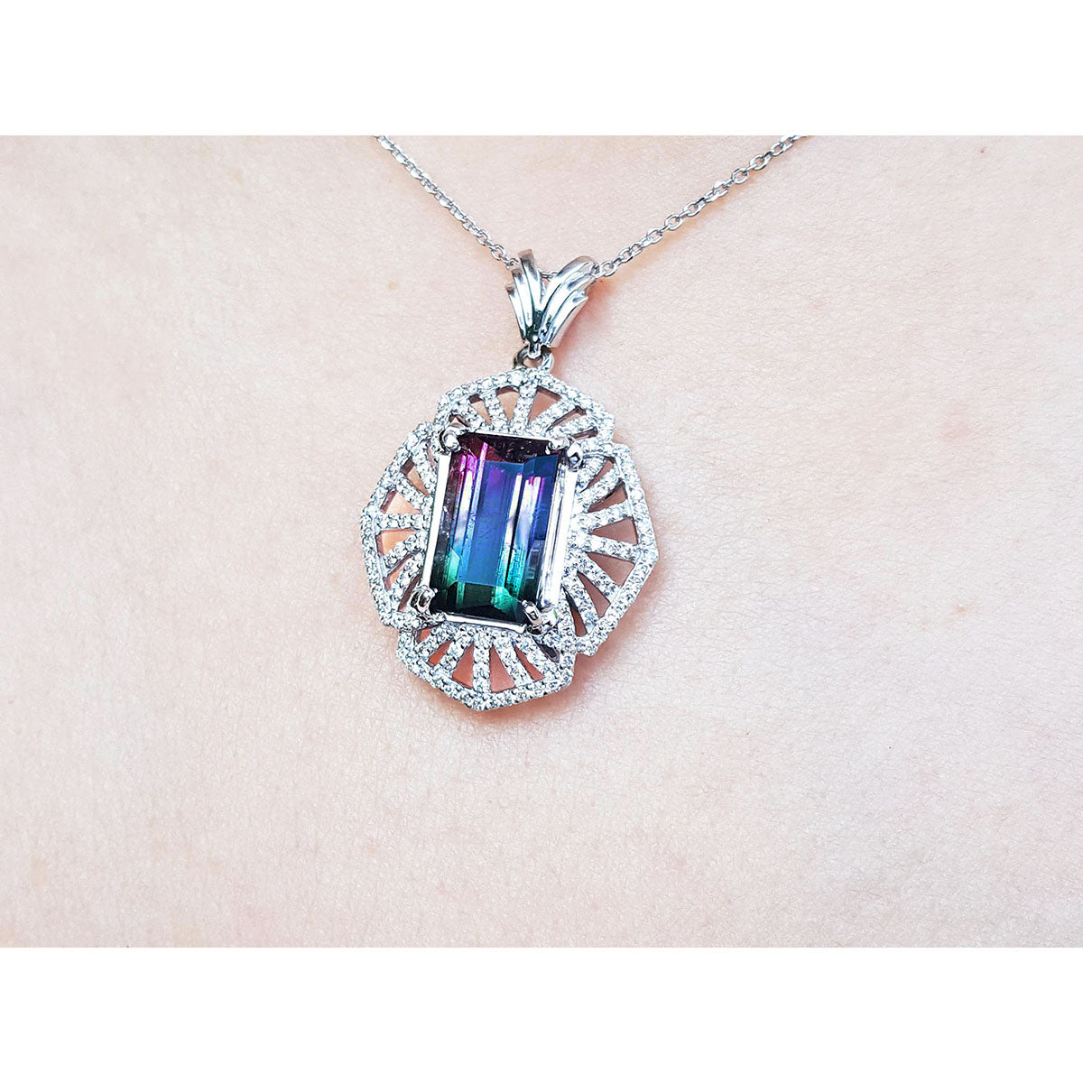 A natural bicolor tourmaline pendant in white gold and diamonds on a pink skin background.