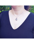 A woman wearing a black top and a white gold chain with a tourmaline pendant on a natural background.