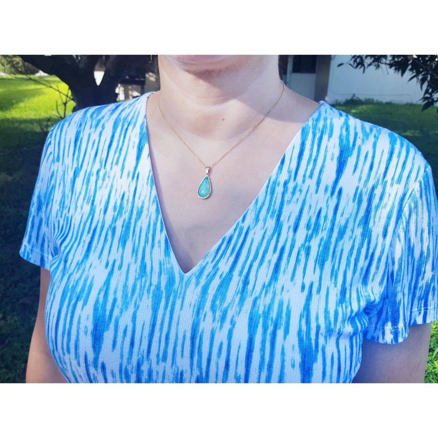 Person wearing a blue and white tie-dye shirt with a necklace outdoors.