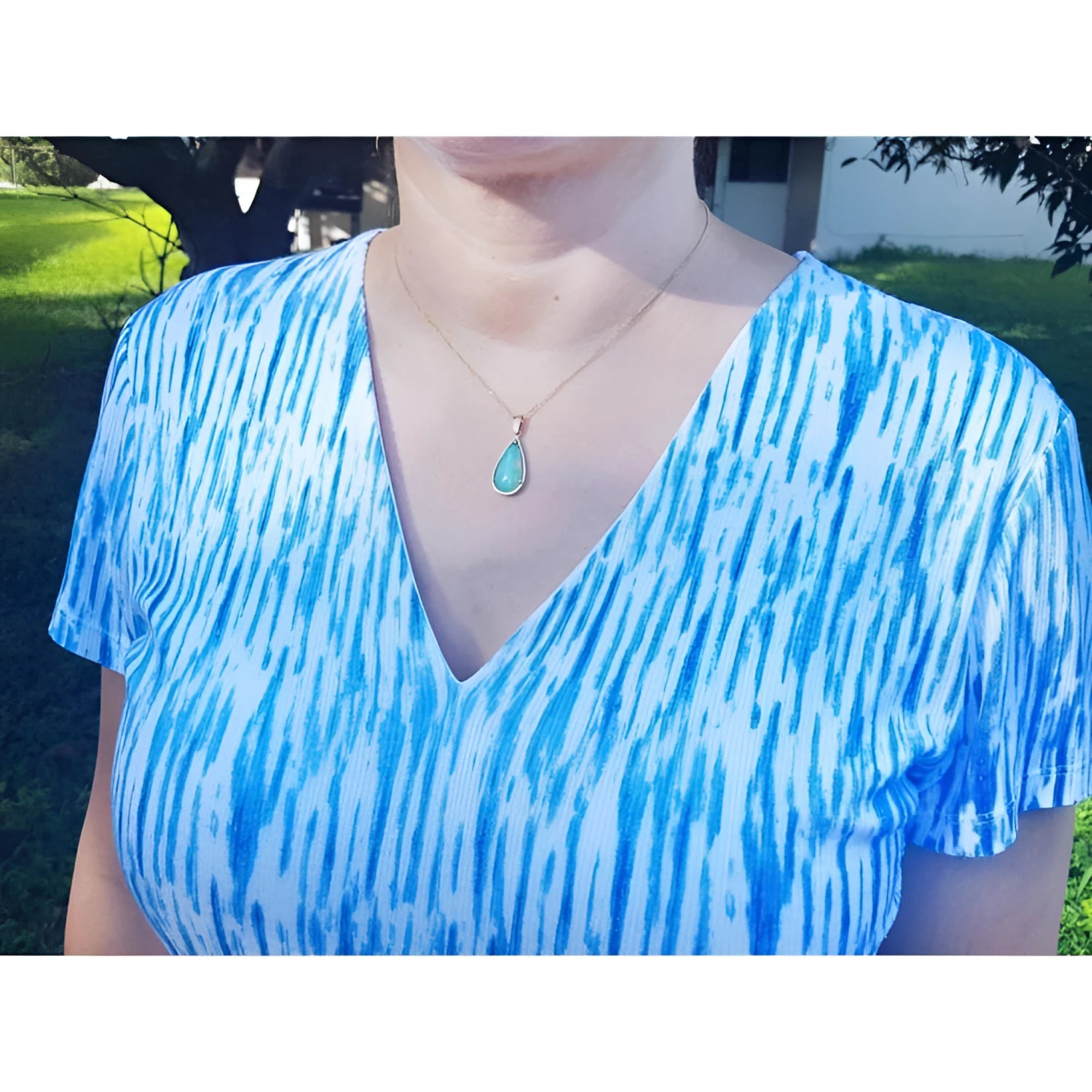 Ethiopian opal pear pendant necklace with blue-violet play-of-color in 14K yellow gold on a woman.