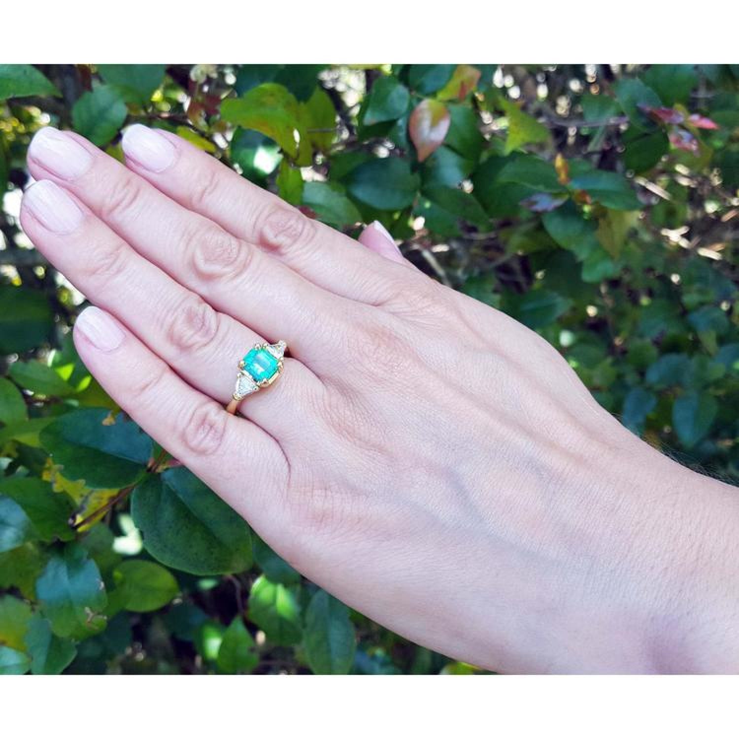 1.51 ct. emerald and trillion cut diamonds ring in 18k gold on a hand.