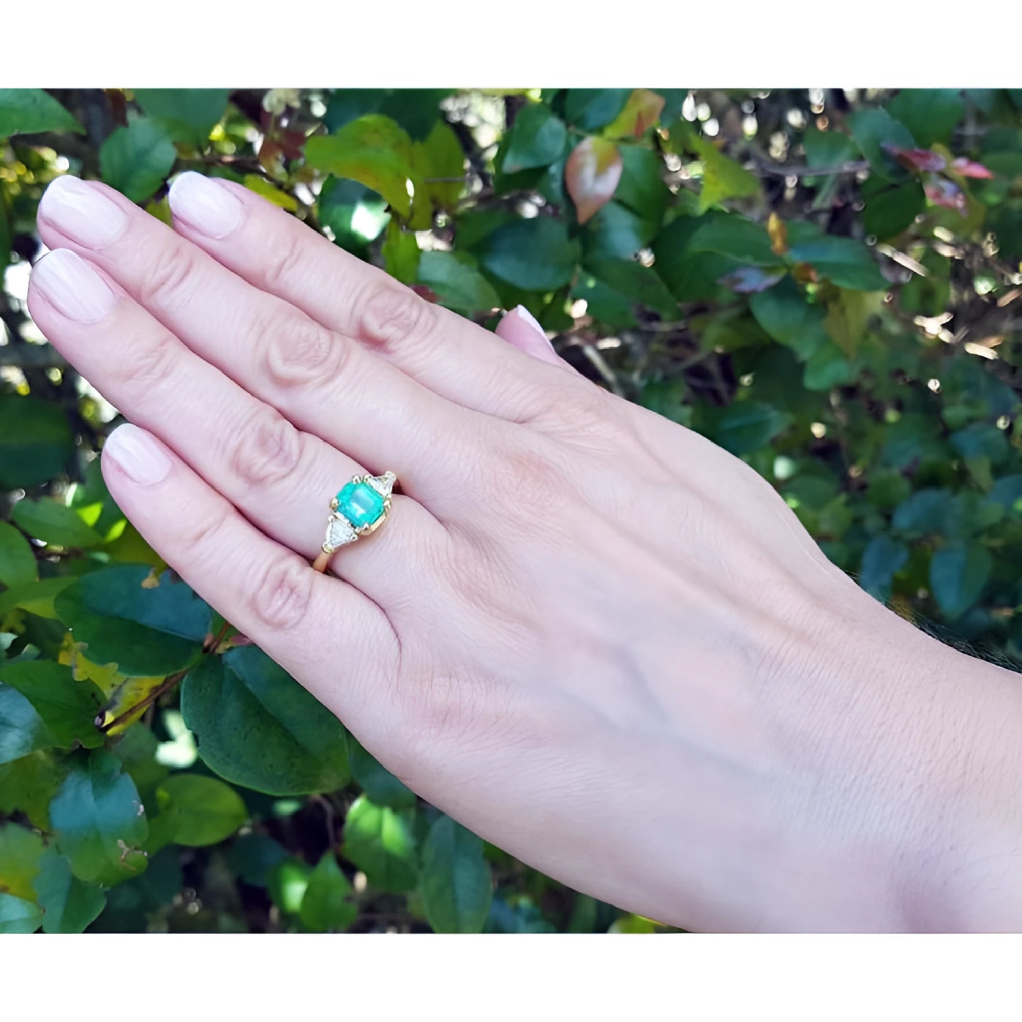 1.51 ct. emerald and trillion cut diamonds ring in 18k gold on a hand.