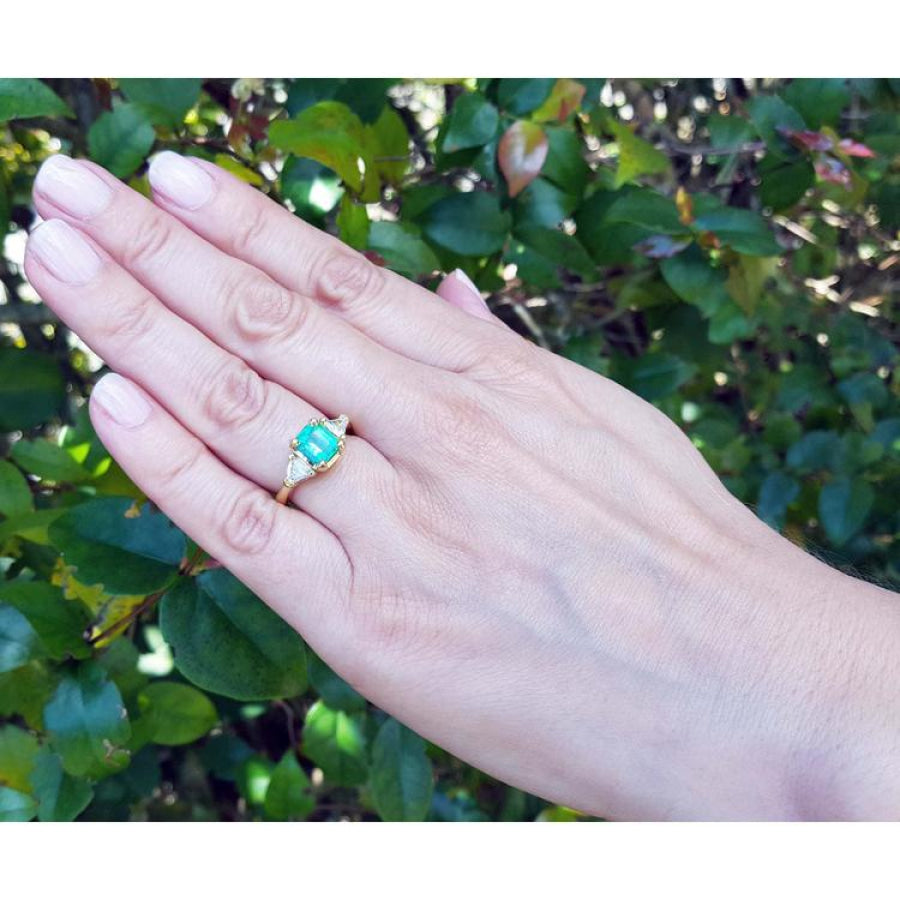 1.51 ct. emerald and trillion cut diamonds ring in 18k gold on a hand.