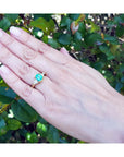 1.51 ct. emerald and trillion cut diamonds ring in 18k gold on a hand.