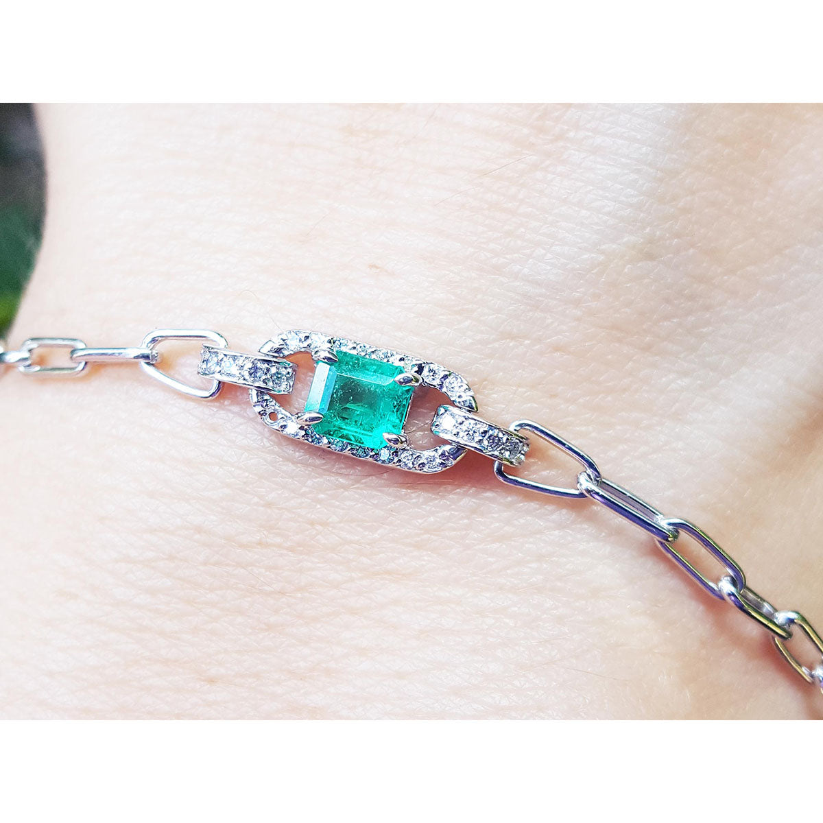 A paper clip bracelet style whit a halo natural diamond surrounding a genuine colombian emerald on a wrist.