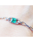 A paper clip bracelet style whit a halo natural diamond surrounding a genuine colombian emerald on a wrist.