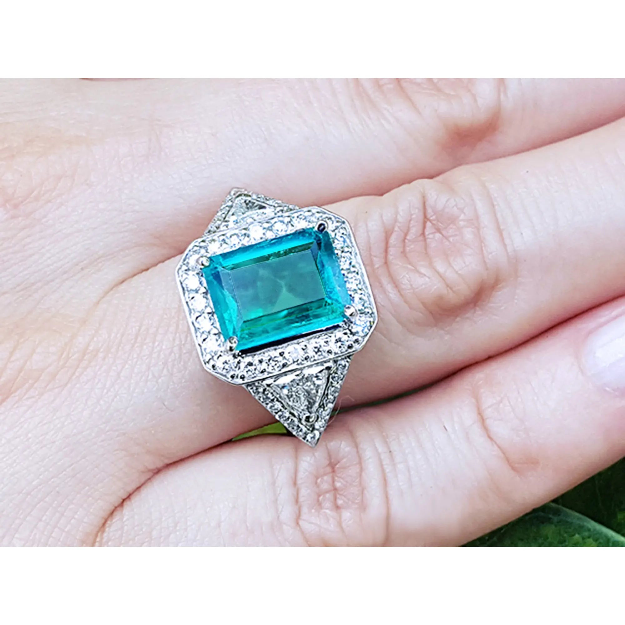 Toma fotografica mas cercana de un anillo con esmeralda cuadrada rodeada de diamantes en una mano.