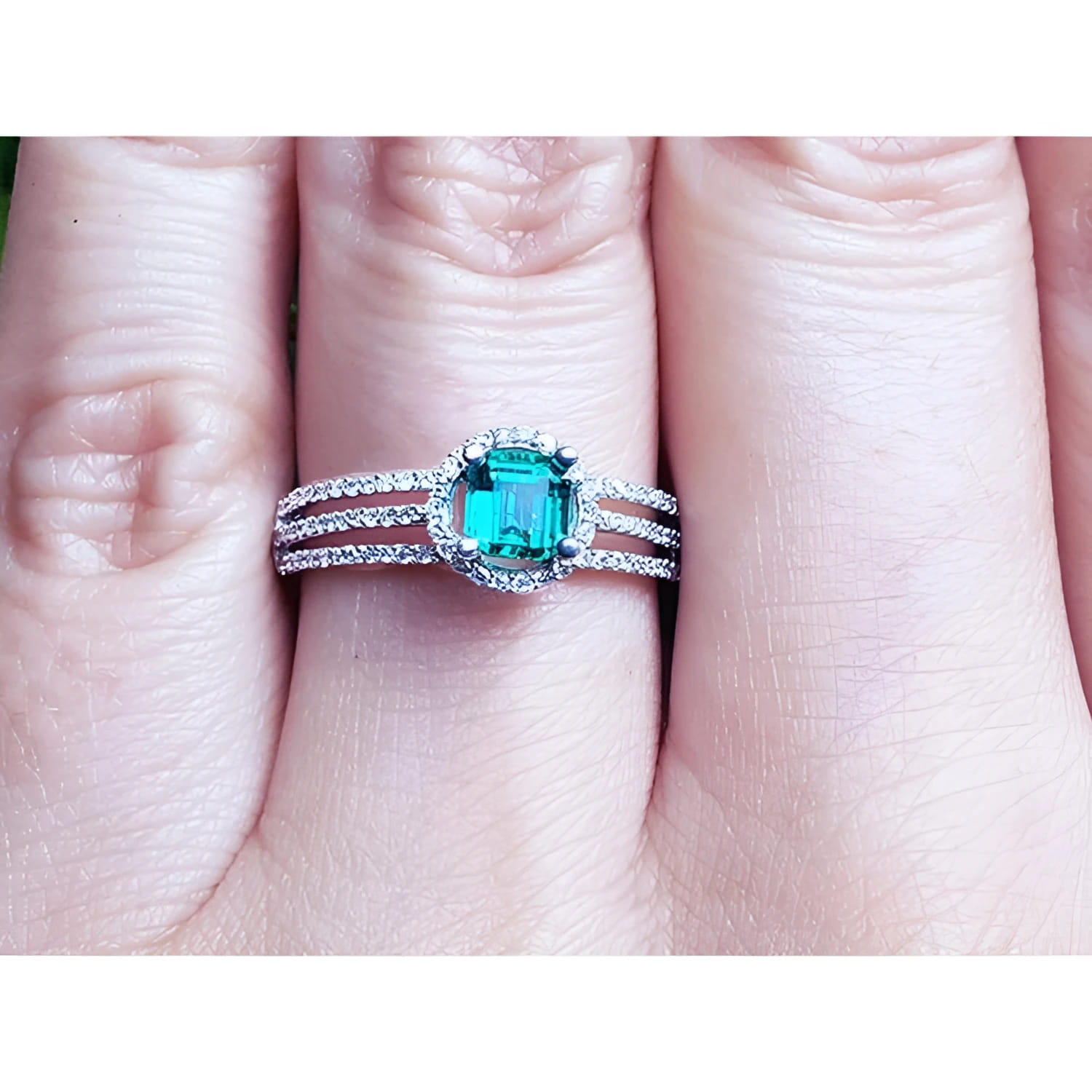 A white gold emerald ring with diamonds accents on a person's finger.