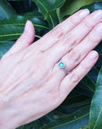 A hand wearing an emerald engagement ring in white gold on a leafy background.