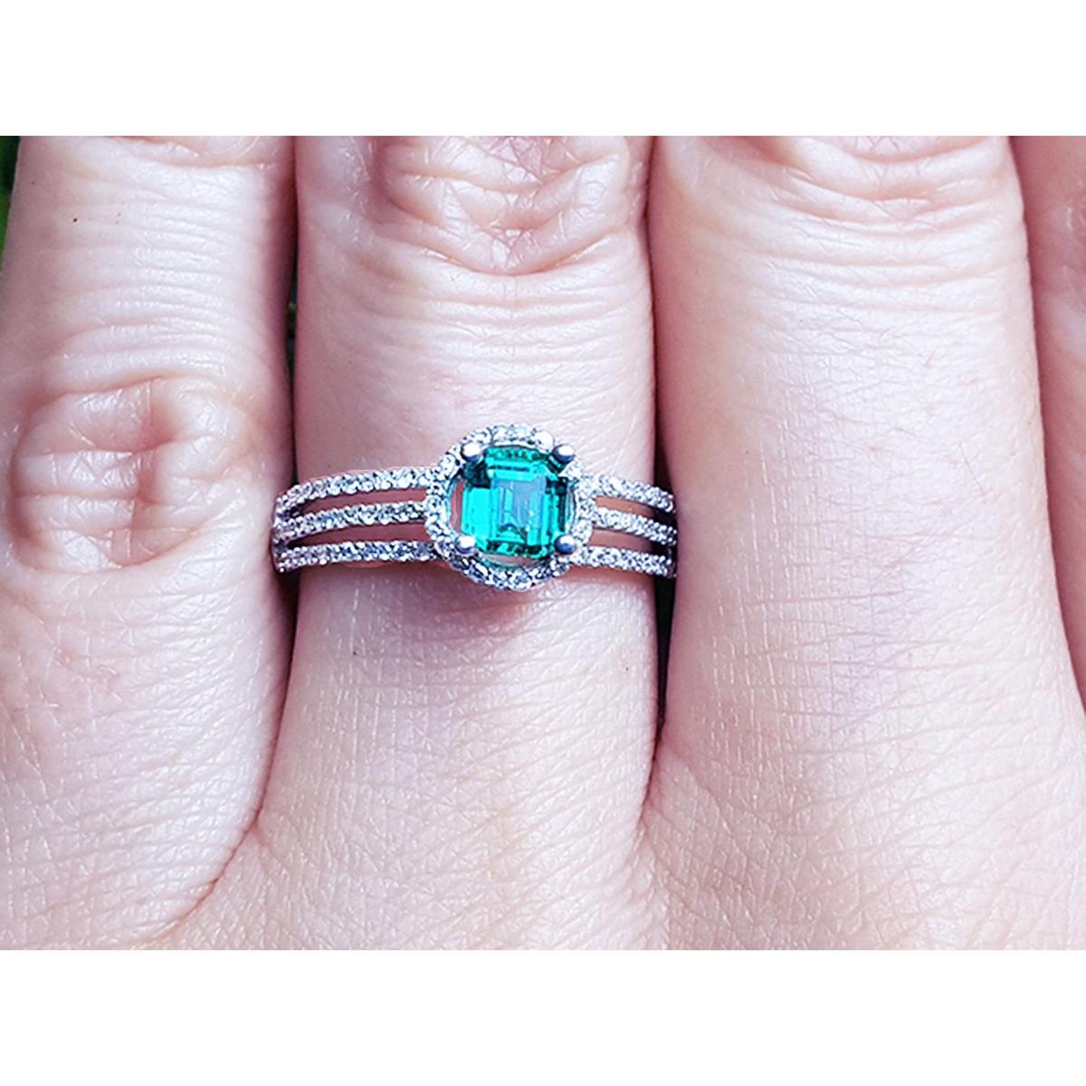 A white gold emerald ring with diamonds accents on a person's finger.