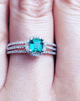 A white gold emerald ring with diamonds accents on a person's finger.