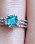 A Muzo Colombian emerald engagement ring on a finger.