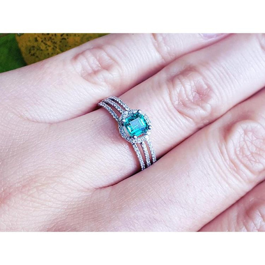 Emerald engagement ring with halo diamonds on a 14K white gold triple-row band, worn on a finger.