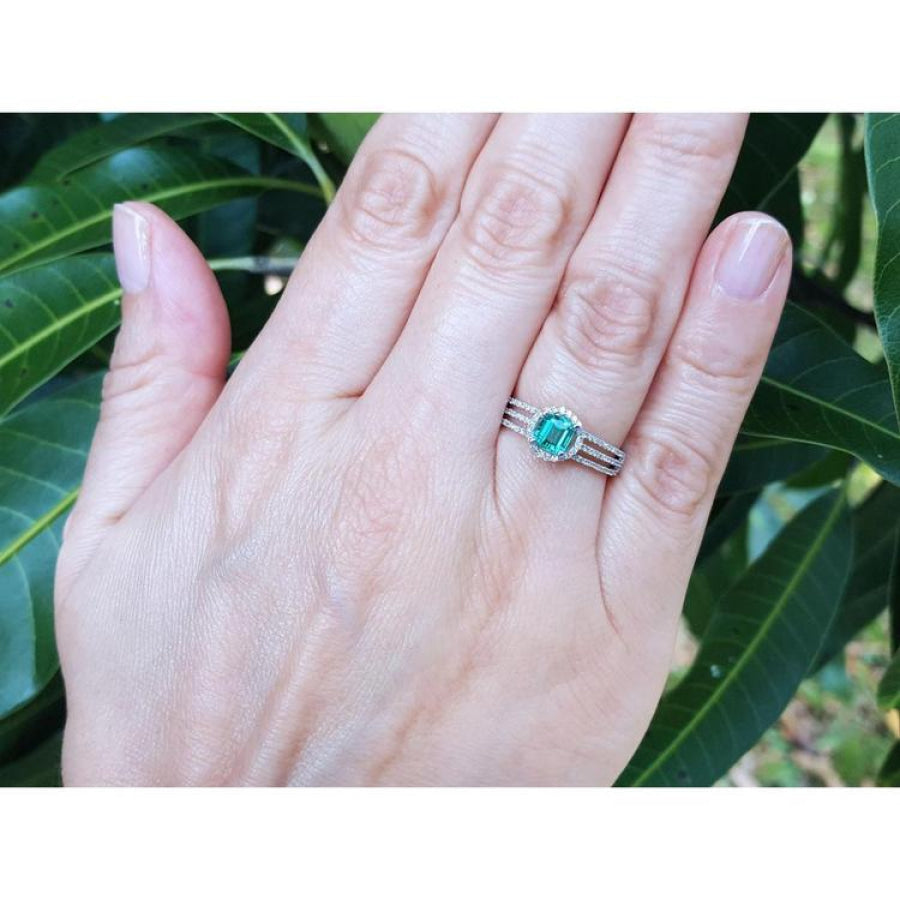 Emerald engagement ring with halo diamonds on a 14K white gold band, worn on a hand.