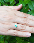 Hand wearing a ring with a green gemstone against a green leafy background