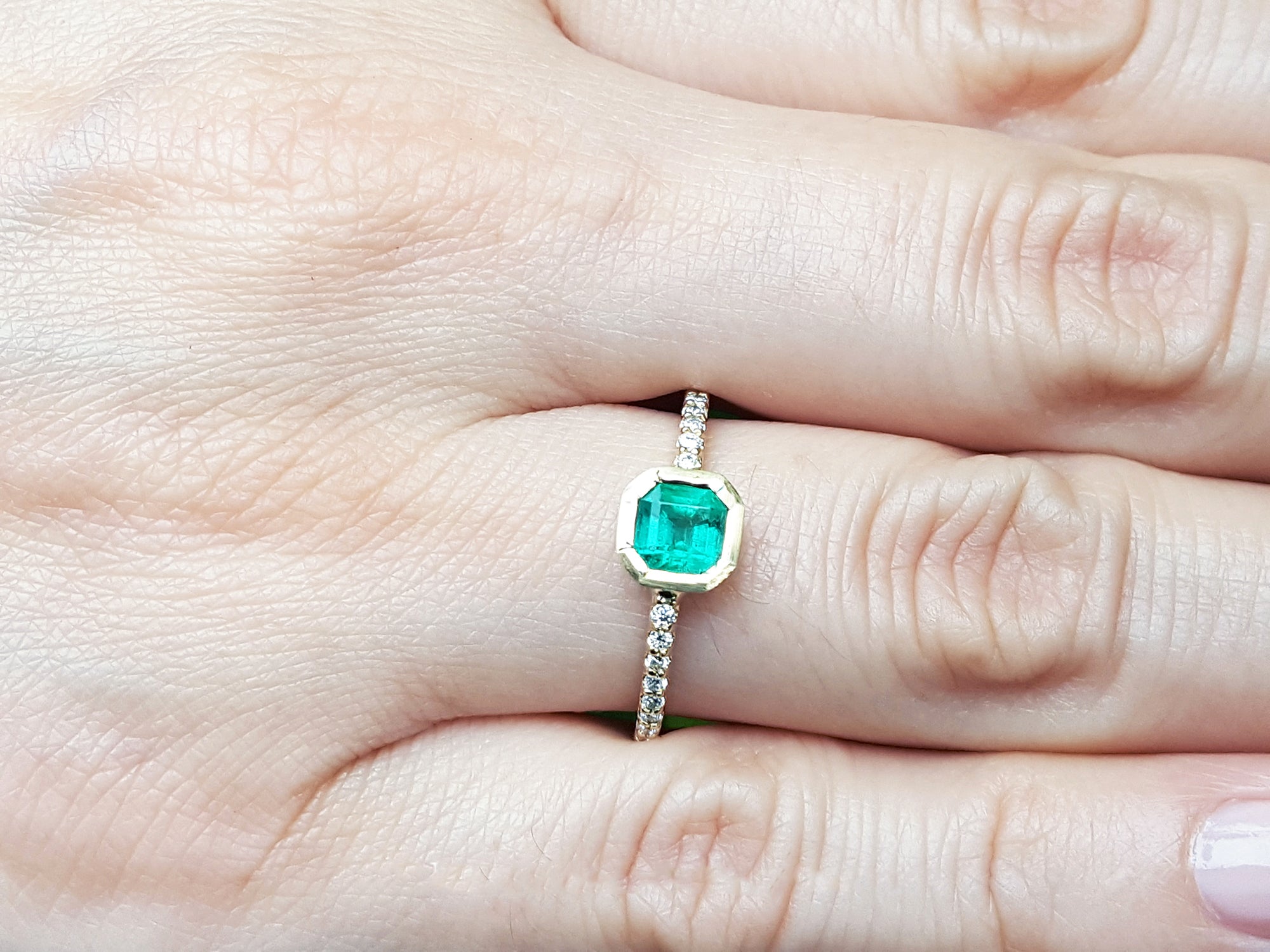 Emerald bezel set ring on a finger.
