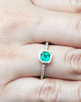 Emerald bezel set ring on a finger.