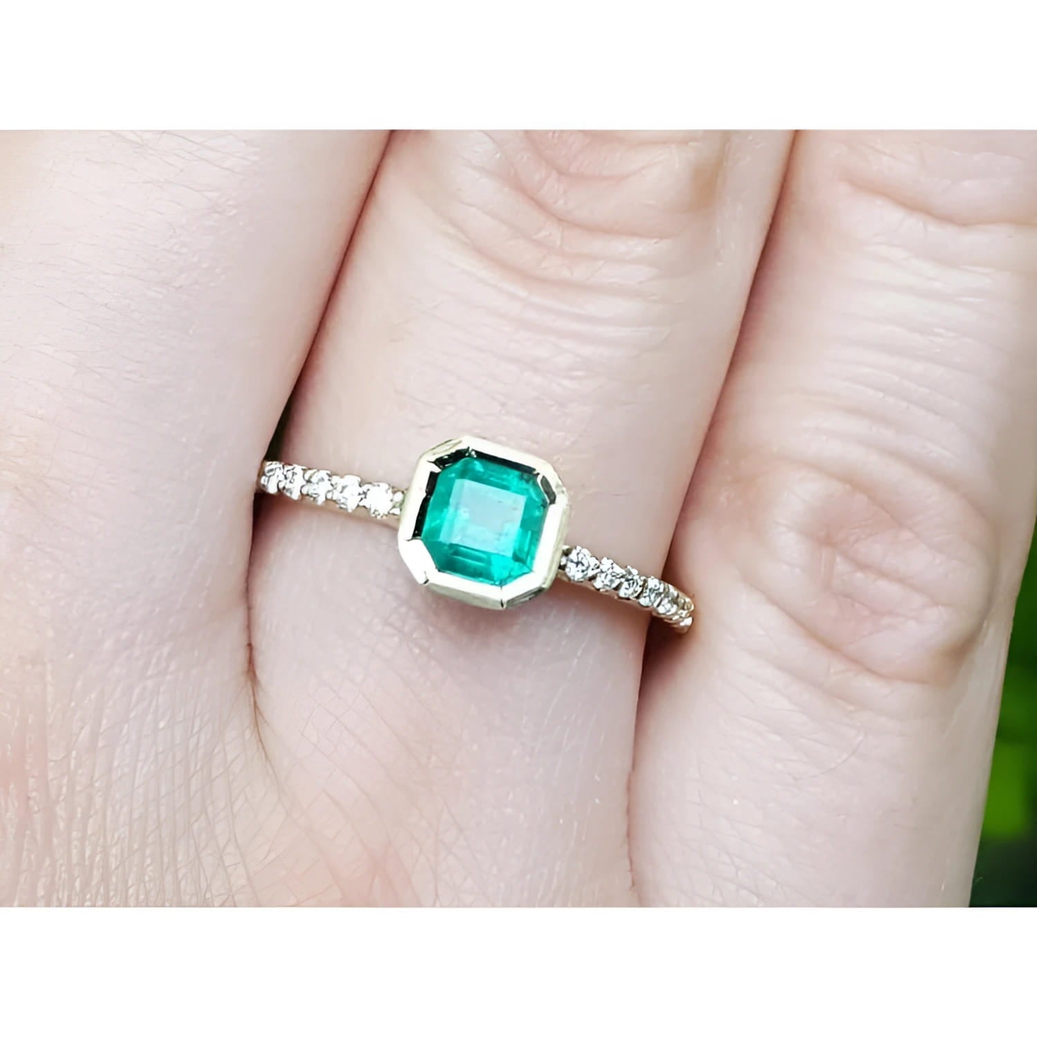A 14k yellow gold colombian emerald ring bezel set with accent diamonds on a finger.