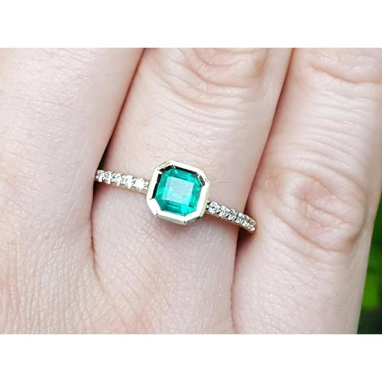 A 14k yellow gold colombian emerald ring bezel set with accent diamonds on a finger.