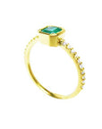A yellow gold ring with a bezel set emerald in a partial side view on a white background.
