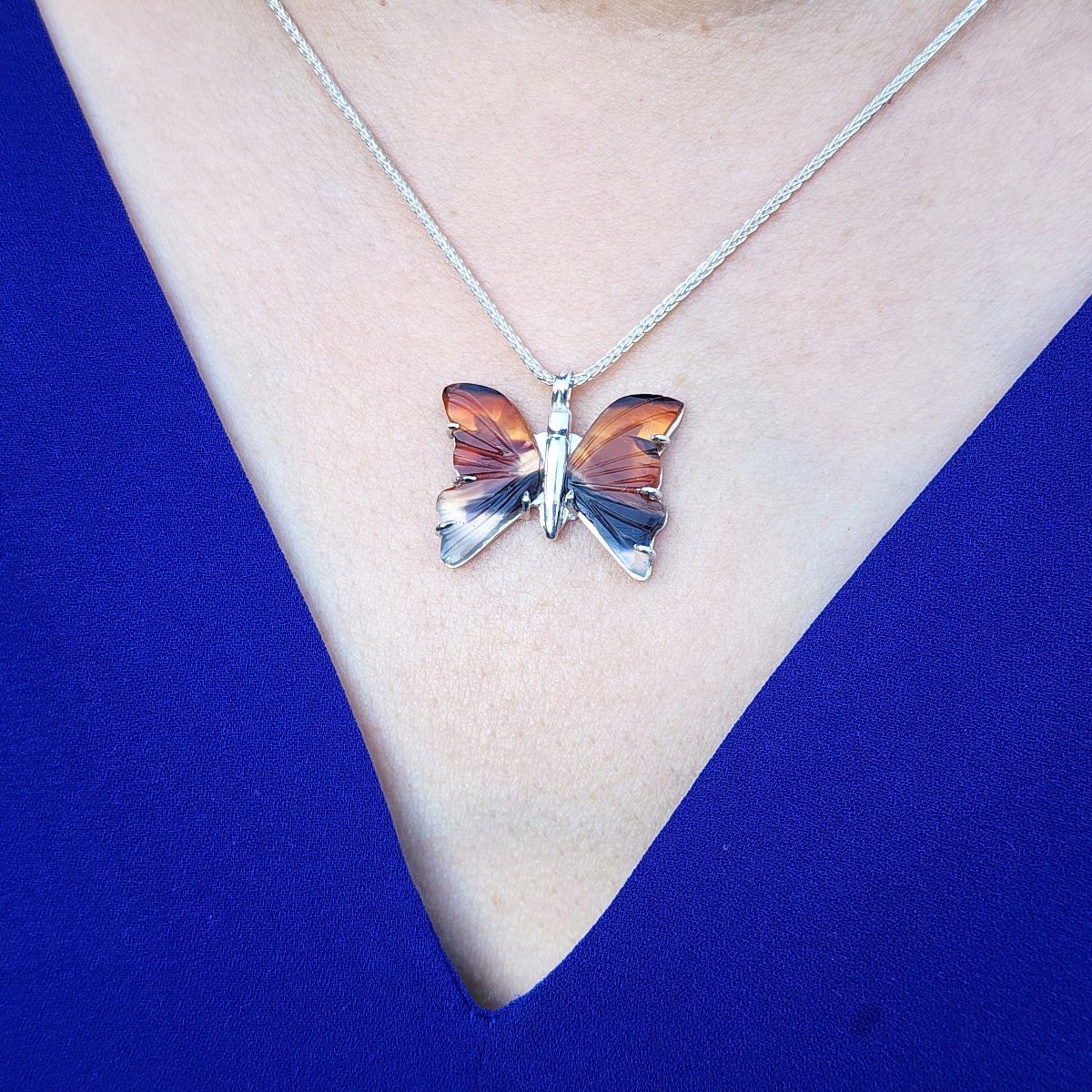 Agate butterfly pendant necklace on a person&#39;s neck against a blue background