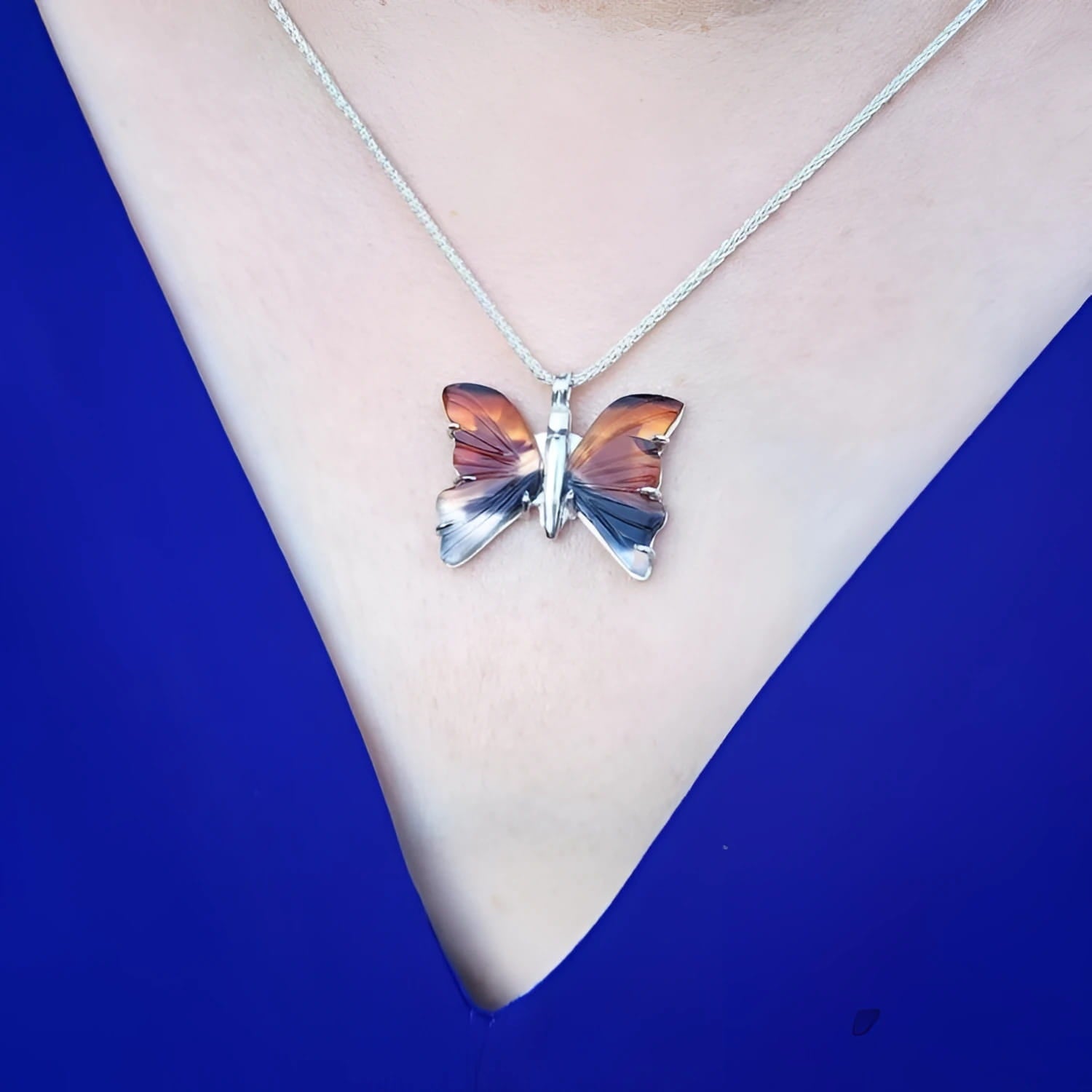Sterling silver agate butterfly pendant necklace with orange, brown, and black hues on a blue top.