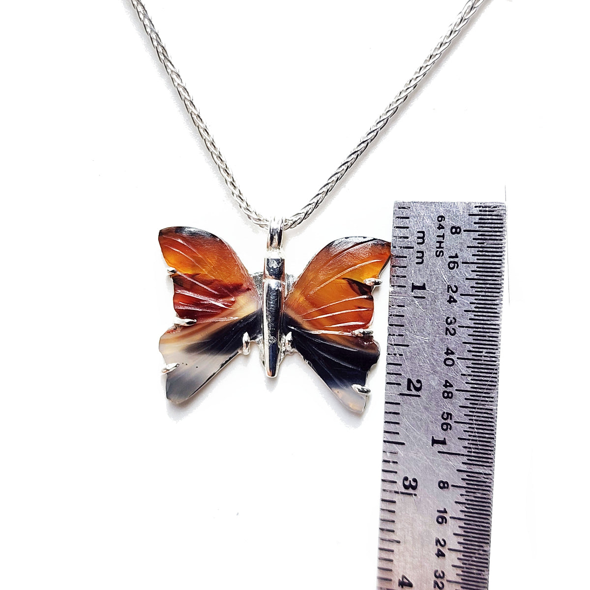 Butterfly-shaped pendant on a chain with a ruler for scale on a white background