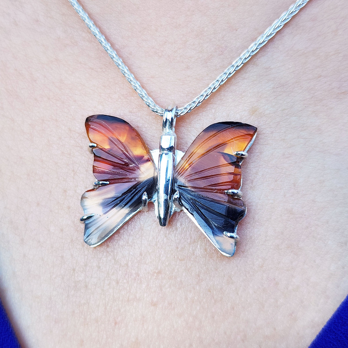 Butterfly-shaped agate pendant on a chain against a skin background