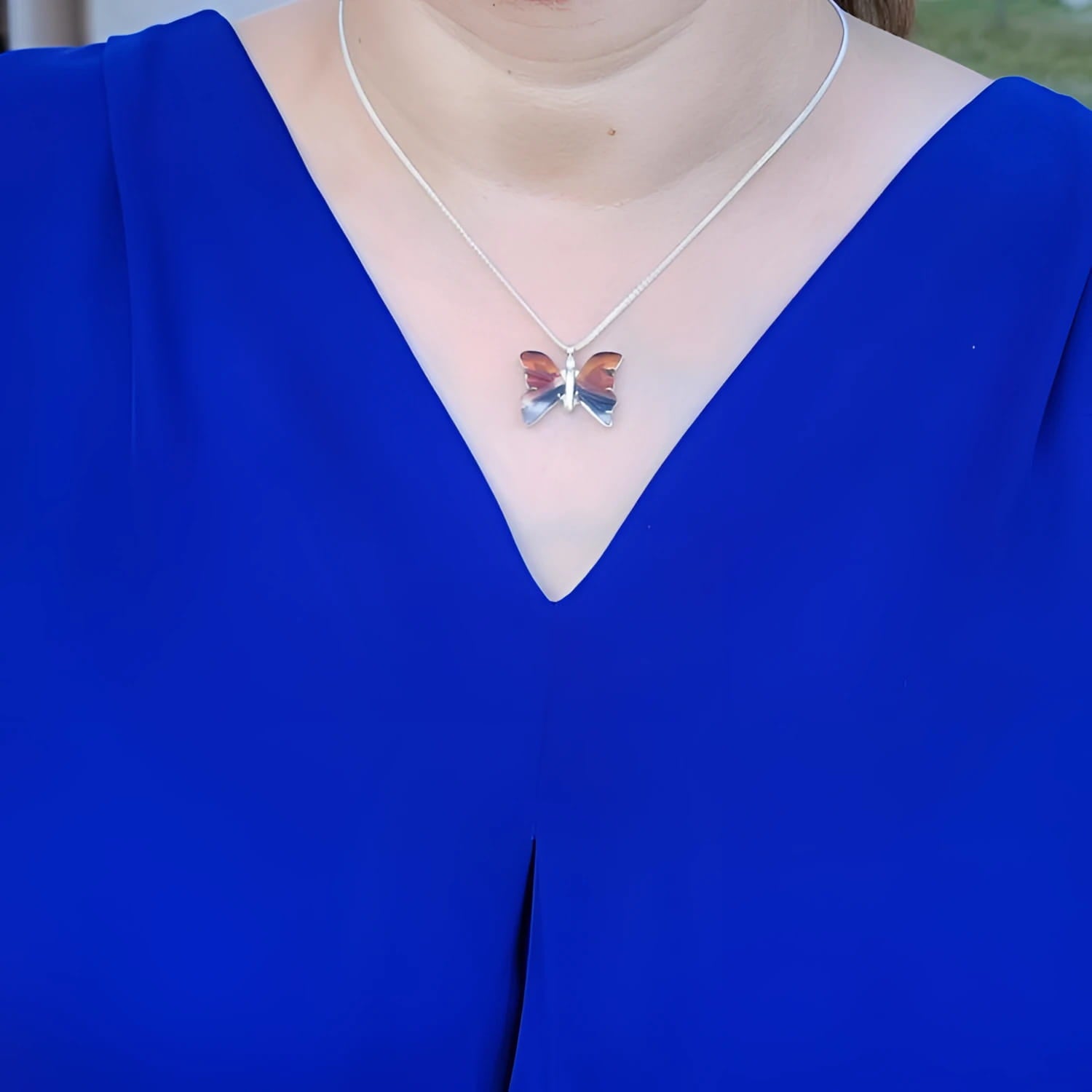 Sterling silver agate butterfly pendant necklace with orange, brown, and black hues, worn on a blue top.