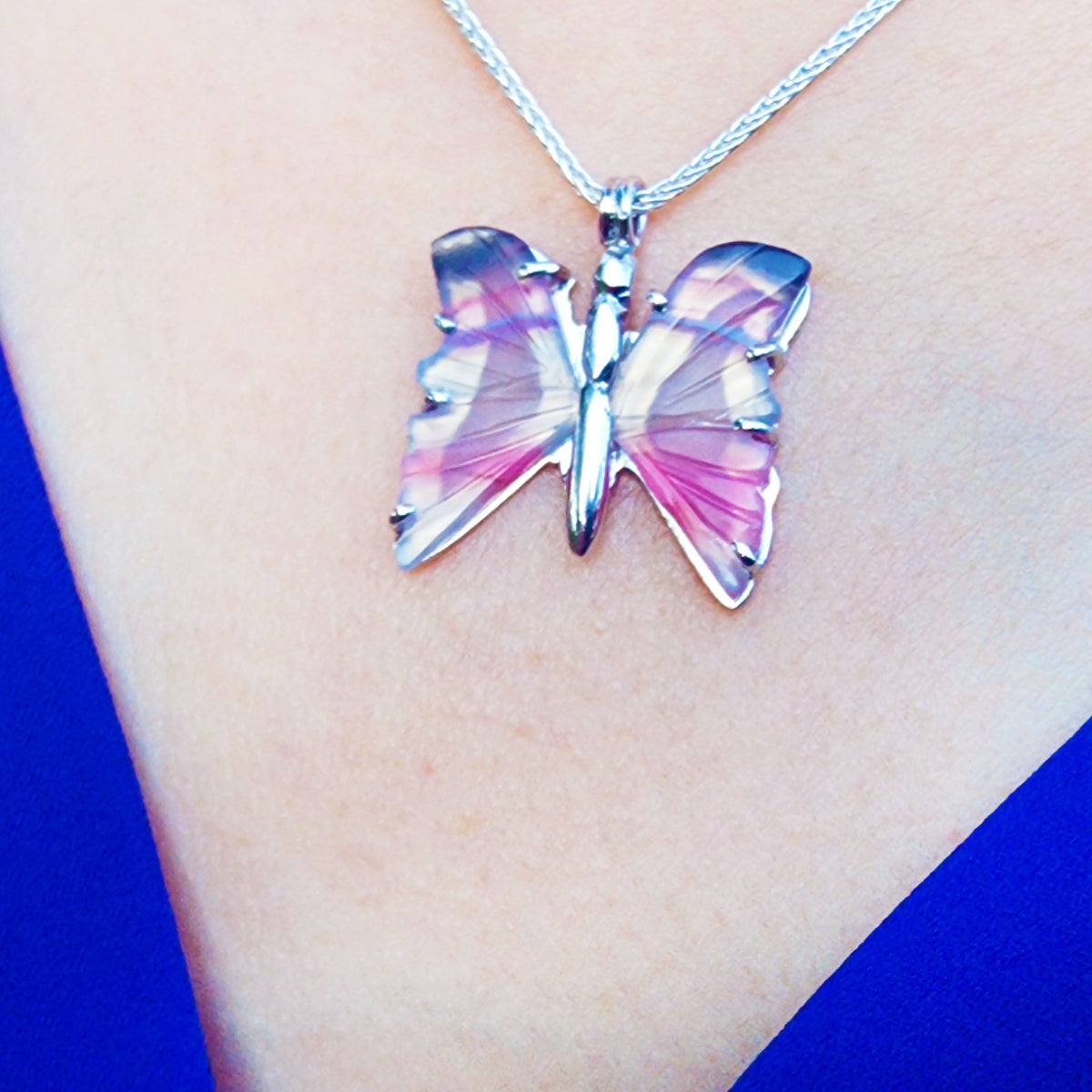 Butterfly-shaped agate silver necklace on a person&#39;s neck with a blue background