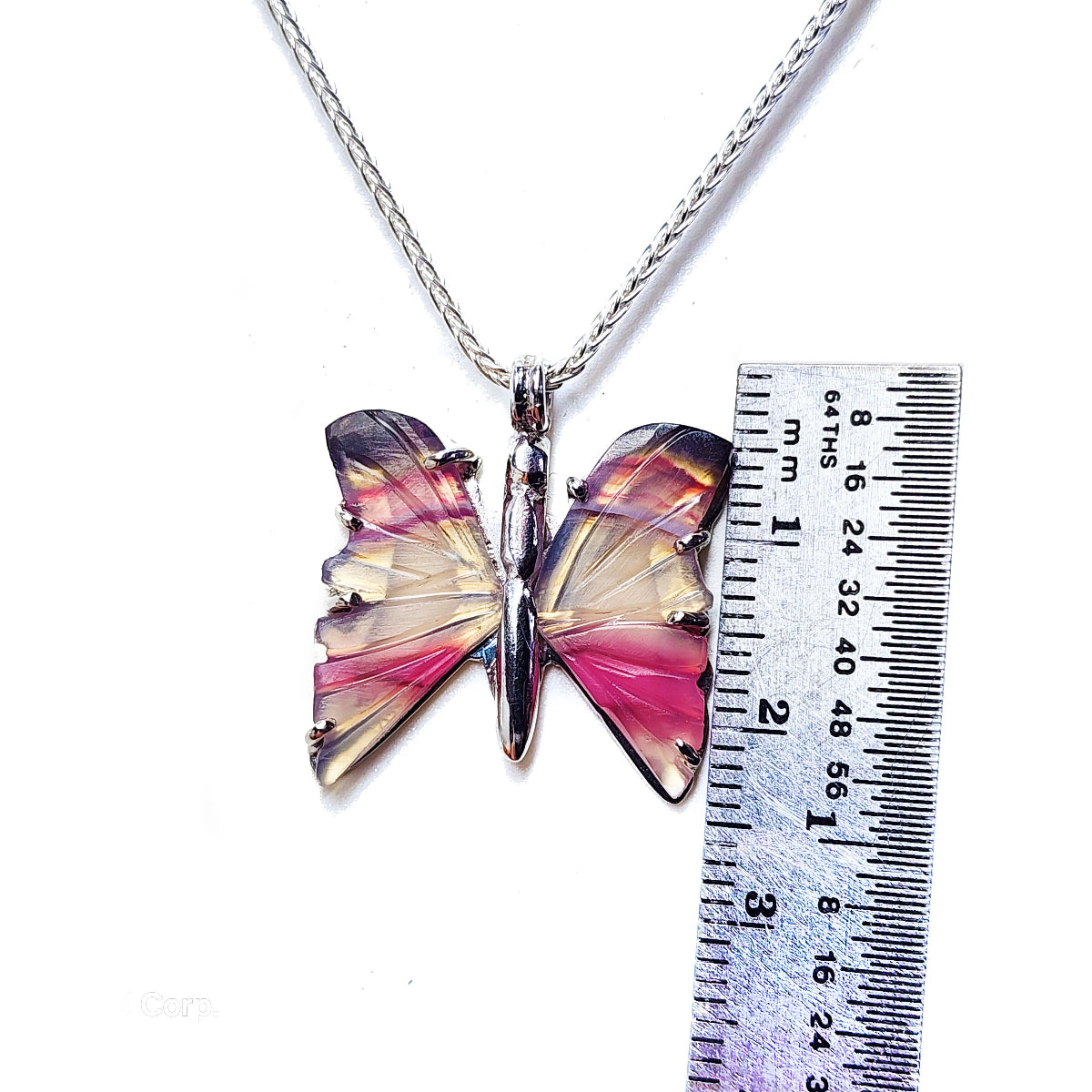 Butterfly-shaped hand carved agate pendant on a silver chain next to a ruler for scale