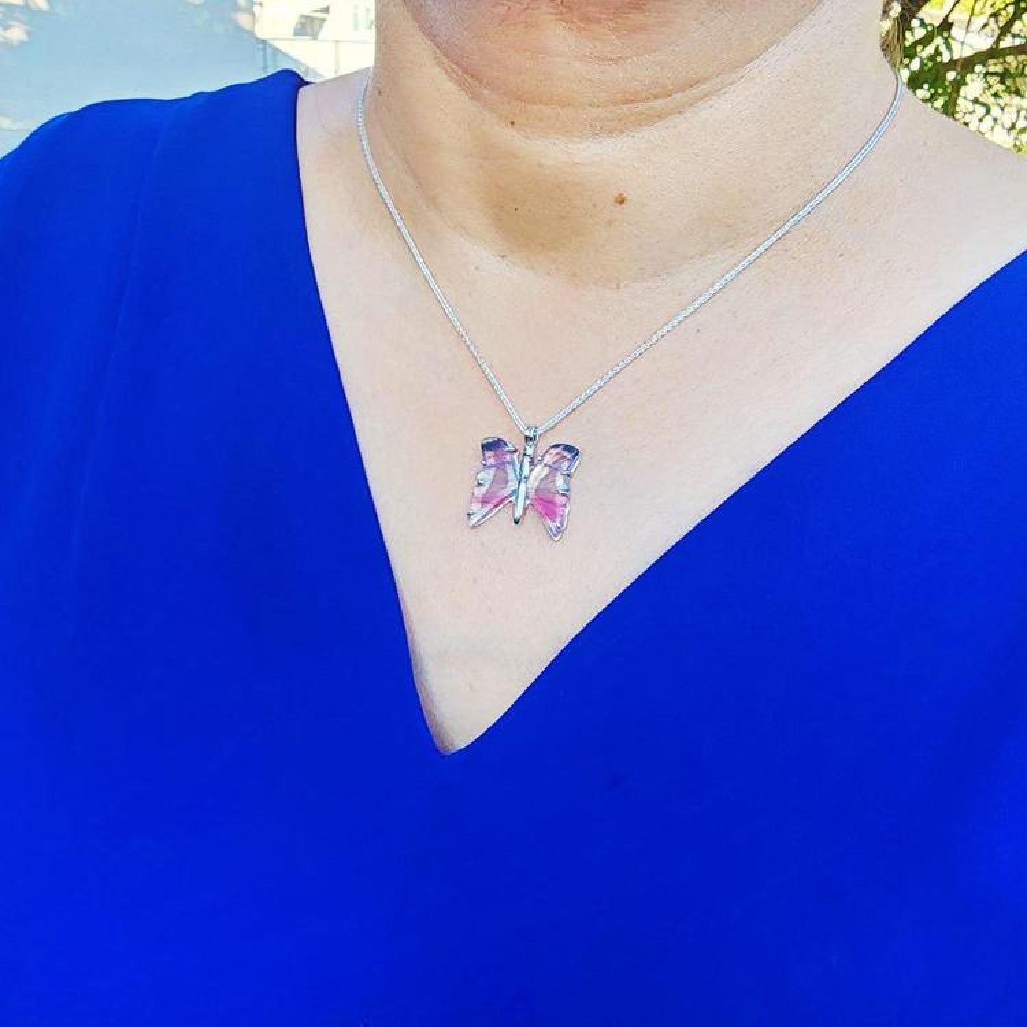 Sterling silver butterfly agate pendant necklace with rich pink wings on a woman's blue top.