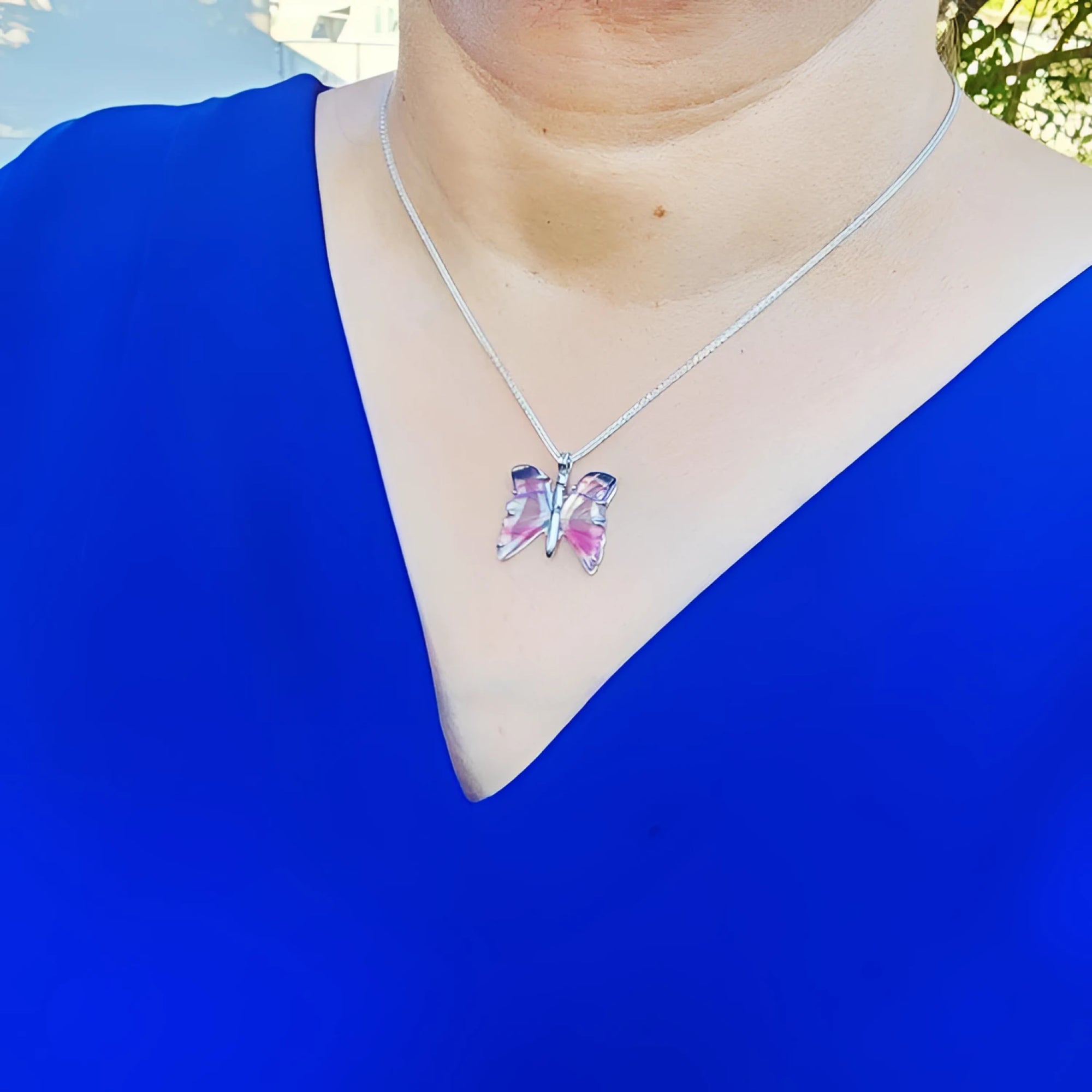 Sterling silver butterfly agate pendant necklace with rich pink wings on a woman's blue top.