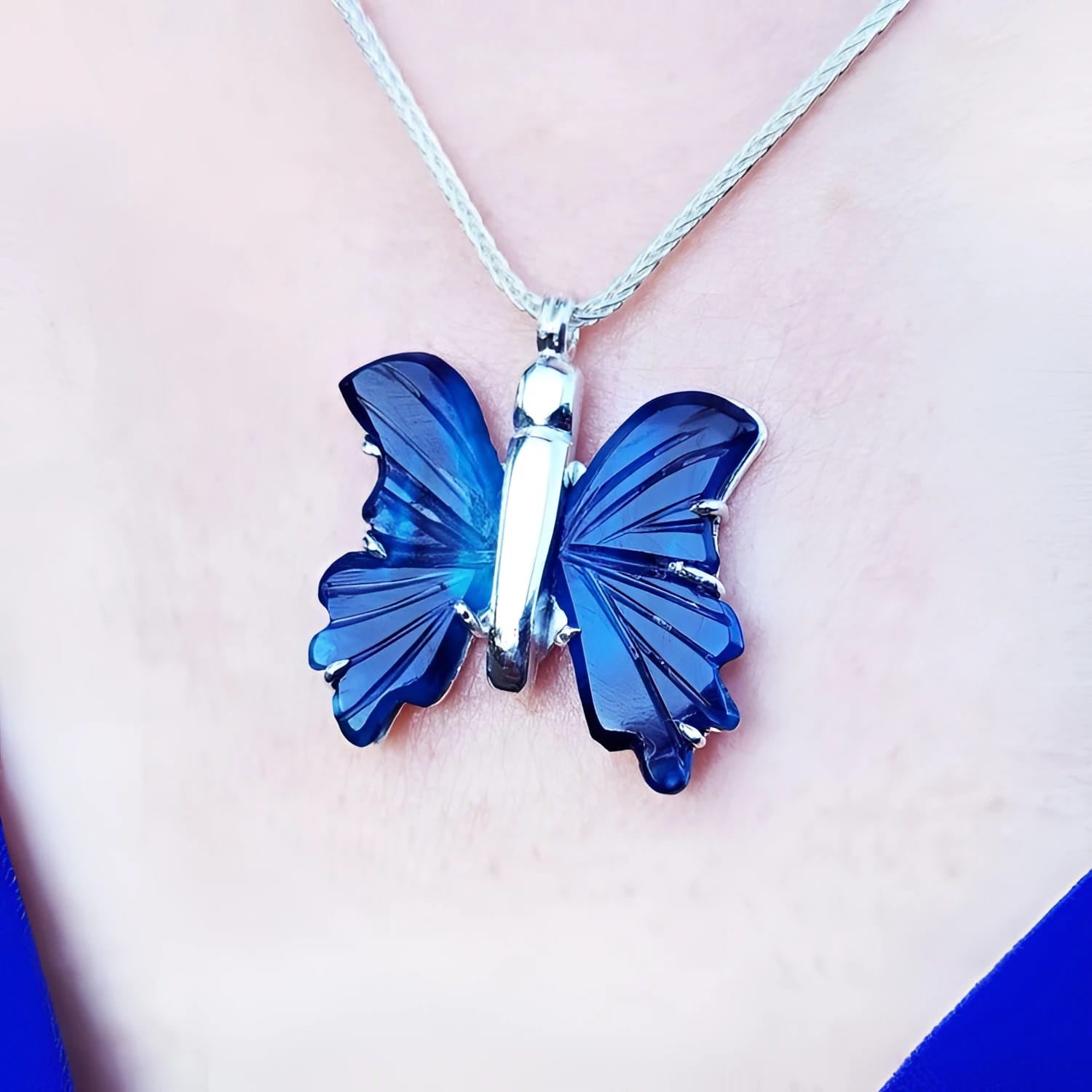 Dark blue natural agate butterfly pendant with silver setting on a silver chain, worn on a person.